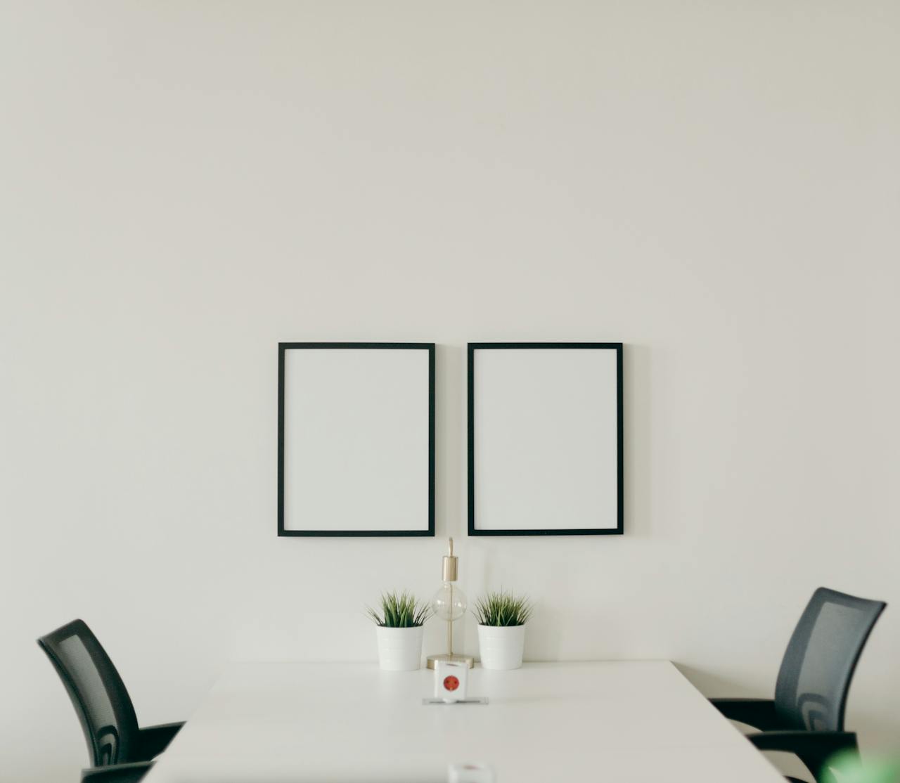 Elegant minimalist home office with white desk, black chairs, and decorative plants, emphasizing simplicity.